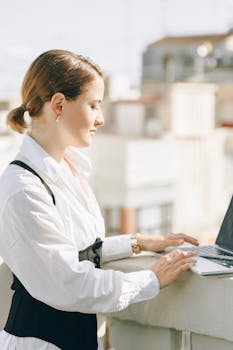 A businesswoman working on her laptop outdoors, focusing on her tasks in the sun.