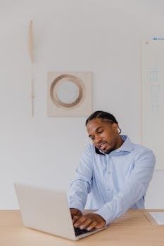 Businessman in office working on laptop and phone call. Professional attire and modern setting.