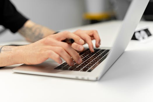 Close-up of tattooed hands typing on a laptop keyboard, showcasing productivity.