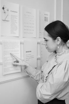 Focused young woman analyzes planning documents on the office wall.