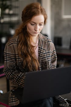 Focused young woman working remotely on her laptop indoors, embracing a casual work style.