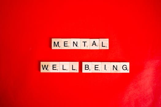 Wooden Scrabble tiles spelling 'mental wellbeing' on a vibrant red background.