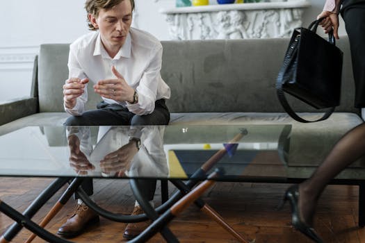 A serious conversation between a man and a woman in a contemporary office setting. The man is sitting while the woman is walking away with a bag.