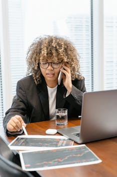 Young business professional analyzing market graphs while on a call at an office desk.