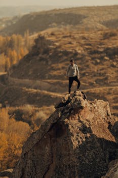 A lone hiker stands atop a rocky peak in İncesu, Kayseri, Türkiye, surrounded by autumn scenery.