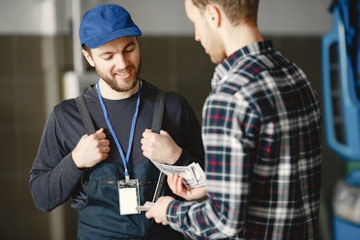 A mechanic in a blue cap receives cash payment from a customer in a plaid shirt, smiling.