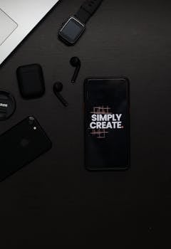 Black flat lay of gadgets including smartphone with 'Simply Create' text, smartwatch, and stylish earpieces.